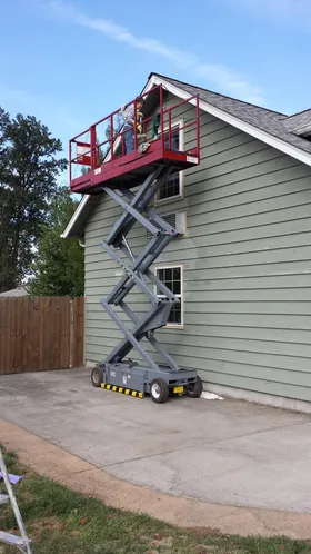 Janey on a scissor lift painting a house at 80